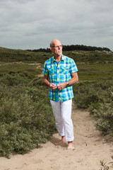 Retired senior man walking outdoors in grass dune landscape. Wea