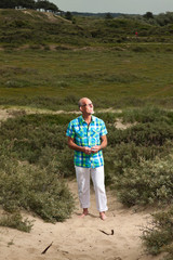 Retired senior man walking outdoors in grass dune landscape. Wea