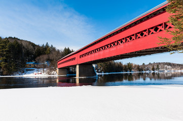 The covered red bridge above the river in winter