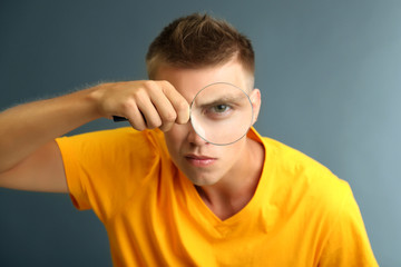 Young man looking through magnifying glass on grey background