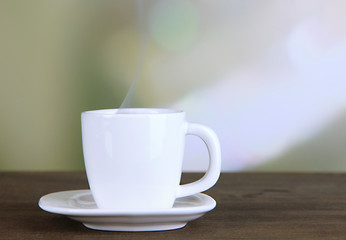 Cup of coffee on wooden table on bright background