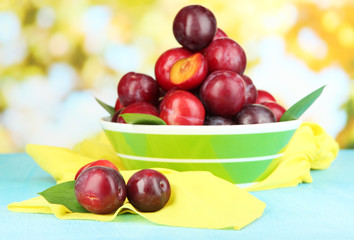 Ripe plums in bowl on wooden table on natural background