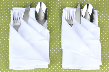 Folded napkin with fork, spoon and knife on color background