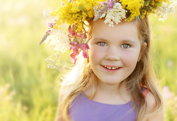 Happy little girl in flower crown on sunny summer meadow