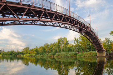 Дугообразный, металлический пешеходный мост через реку