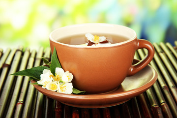 Cup of tea with jasmine, on bamboo mat, on bright background