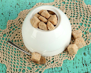 Unrefined sugar in white sugar bowl on wooden background