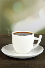 Cup of coffee on wooden table on bright background