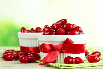 Fresh cornel berries in white cups on wooden table