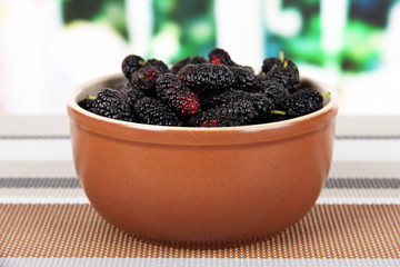 Ripe mulberries in bowl on table in room