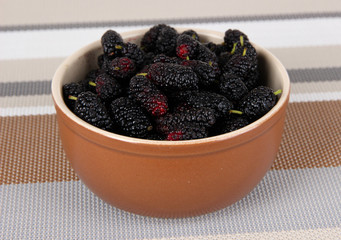 Ripe mulberries in bowl on table in room
