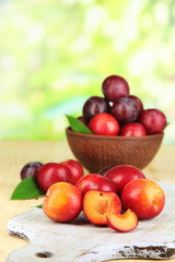 Naklejka na ściany i meble Ripe plums in bowl on wooden table on natural background