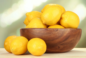 Ripe lemons in bowl on table on bright background