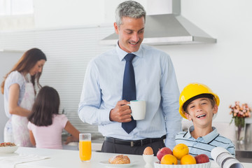 Funny little boy wearing fathers hardhat during breakfast