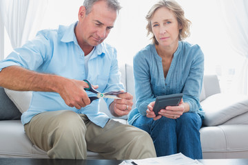 Husband cutting credit card in half with wife looking at camera