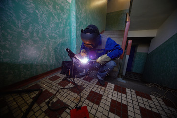Welder in protective suit and mask welds metal pipes