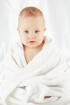Baby sits wrapped in bath towel after bathing