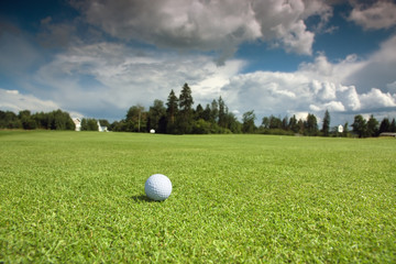Golf ball on the course, green grass, blue sky and white clouds