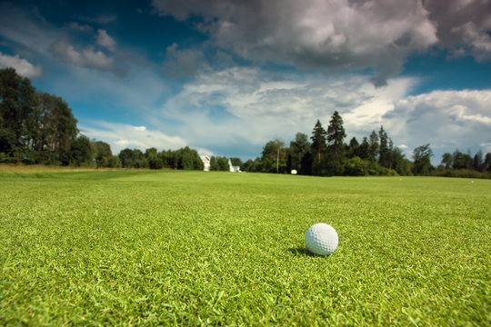 Golf ball on the course, green grass, blue sky and white clouds