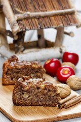 Cinnamon cake on wooden tray. Red apples and nuts in the back