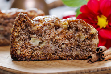 Cinnamon cake on wooden tray. Red apples and nuts in the backgro