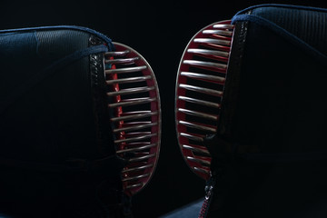 Two kendo helmets facing each other over dark background
