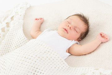 Relaxed baby sleeping in knitted white blanket