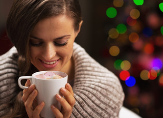 Woman with cup of chocolate with marshmallow near christmas tree