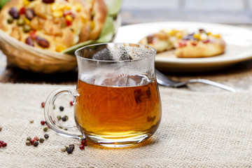 Glass of hot steaming tea, basket of buns in the background