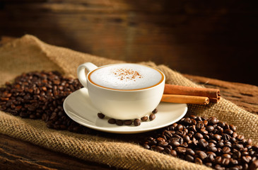 A cup of cappuccino and coffee beans on old wooden background
