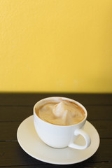 Coffee cup on wooden board with yellow wall as background