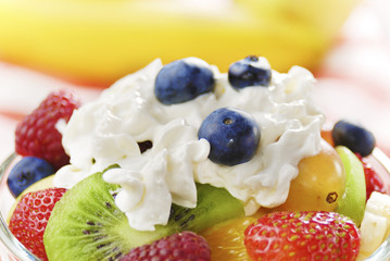 Sweet tasty fruit salad in the bowl with whipped cream