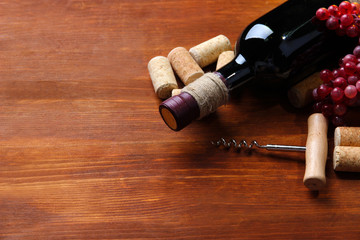 Bottle of wine, grapes and corks on wooden background