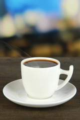 Cup of coffee on wooden table on bright background