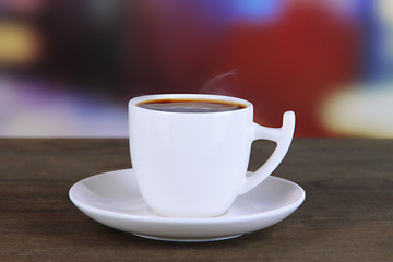 Cup of coffee on wooden table on bright background