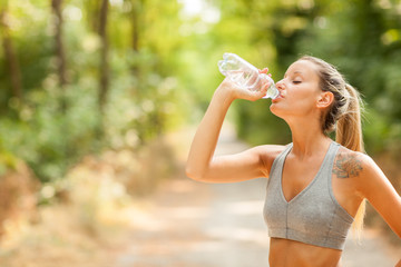 Young woman is drinking water after running session