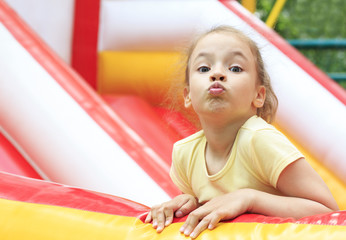 Fototapeta na wymiar Joyful little girl makes a face on a trampoline.