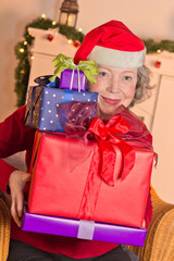 Seniorin mit vielen Geschenken und Weihnachtsmann-Mütze