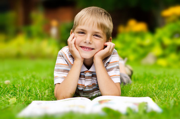 Beauty smiling child boy reading book outdoor on green grass fie - 55350065