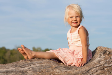Fototapeta na wymiar Cute little girl sitting on old tree