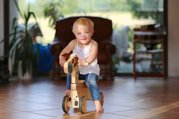 Happy baby learns to ride on a wooden horse on wheels