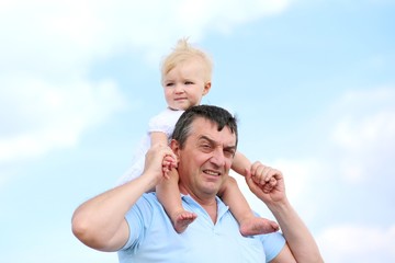 Baby sitting on father shoulder, blue sky at background