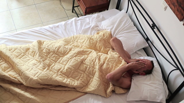 Young man waking up in bed in the morning, top view