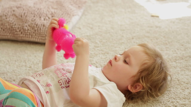 Little girl is playing with toy while laying on floor