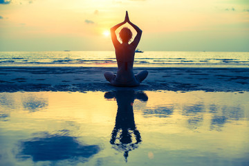 Yoga woman sitting in lotus pose on the beach during sunset