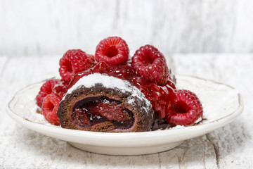 Swiss roll (roulade) with raspberries on white plate. Selective