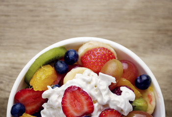 Sweet tasty fruit salad in the bowl with whipped cream