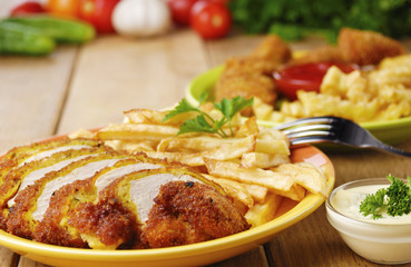 French fries and chicken on the plate on the wooden table