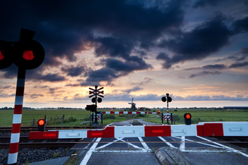 closed rail crossing at sunrise and windmill - obrazy, fototapety, plakaty