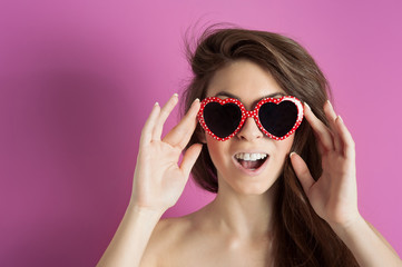 Beautiful girl with heart glasses against pink background.